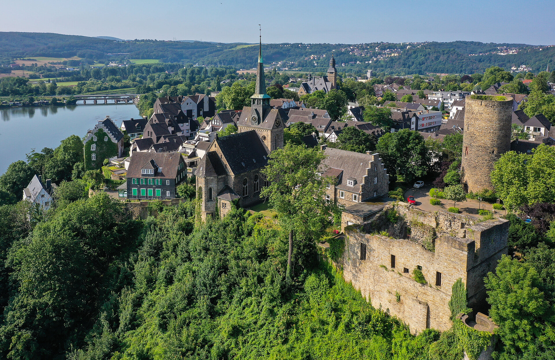 Blick auf die Burgruine aus der Vogelperspektive; am Hang grüne Bäume und oberhalb des Flusses/neben der Ruine der Ort Alt-Wetter mit Häusern