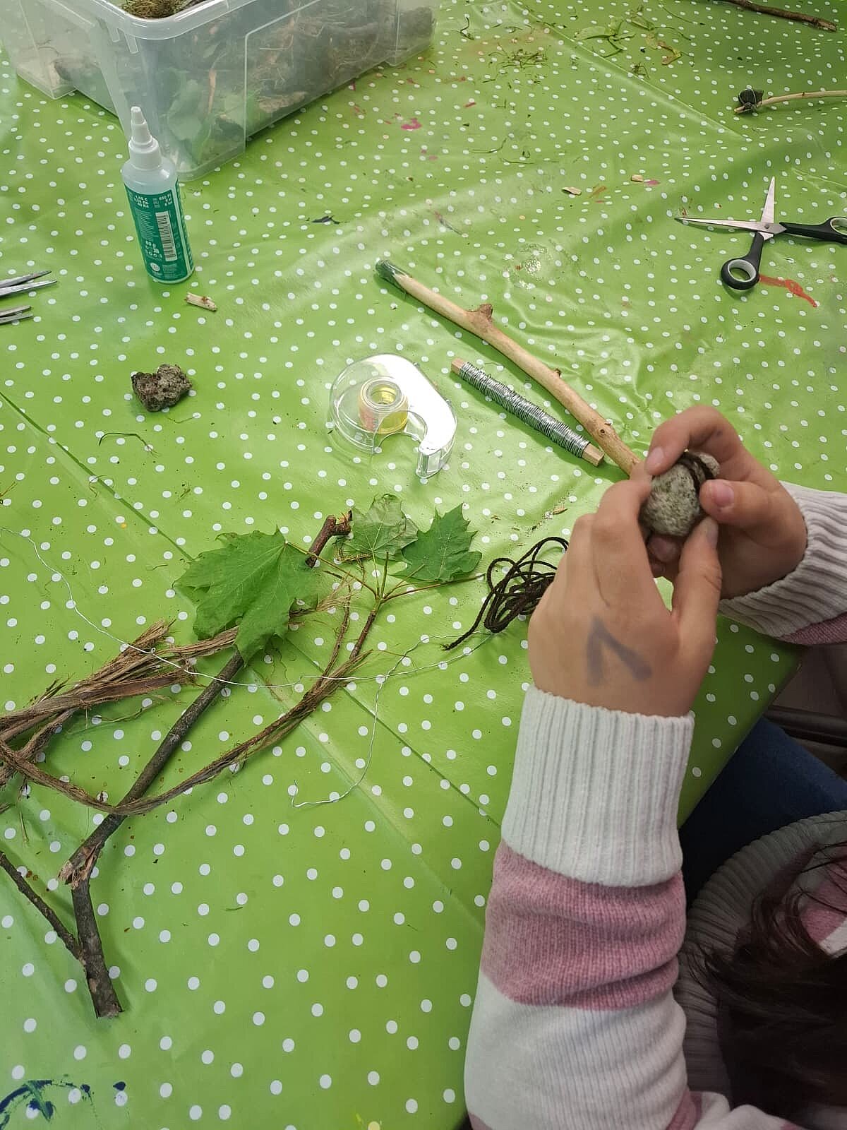 Foto Kunterbunte Kunstwerkstatt Das Foto zeigt, wie ein Kind aus einem Ast und einem Stein einen speziellen Pinsel baut.