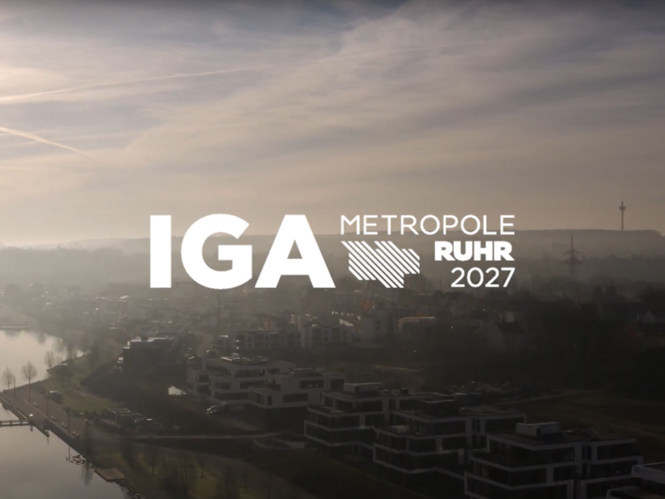 Das Bild zeigt den Schriftzug der IGA Metropole Ruhr 2027 vor einer weiten Landschaftsaufnahme.
