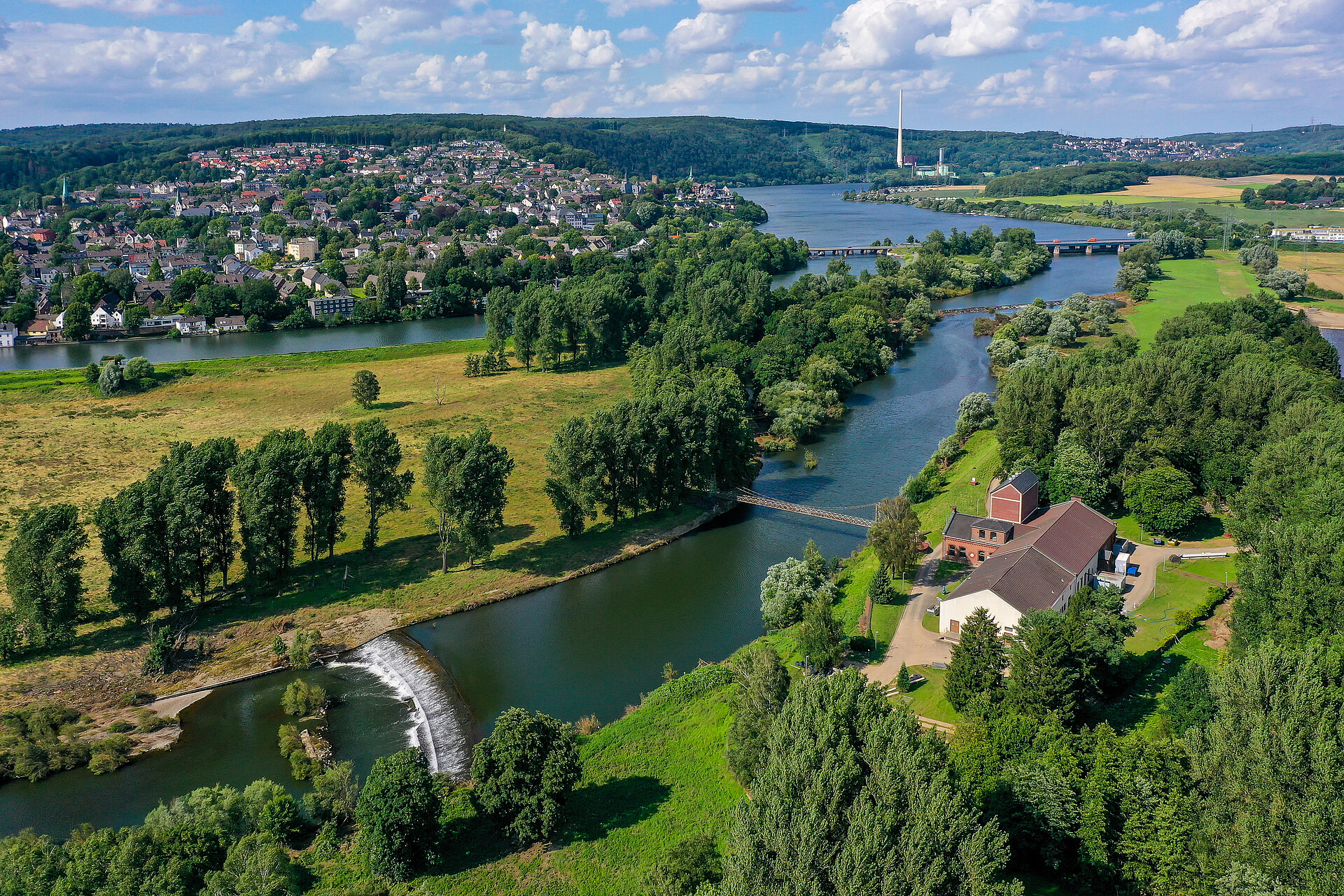 Vogelperspektive auf das ehem. Wasserwerk, daneben direkt die Ruhr im Grünen und im Hintergrund ein Ort mit Wohnhäusern.