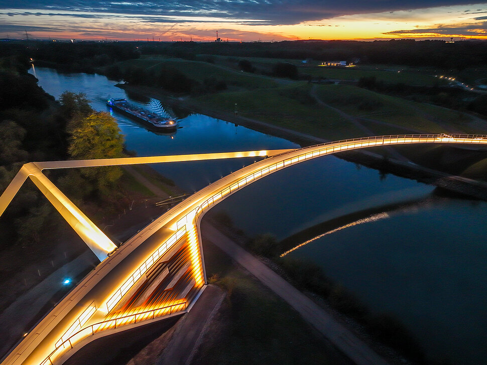 Beleuchtete Fahrradbrücke über Fluß bei Nacht