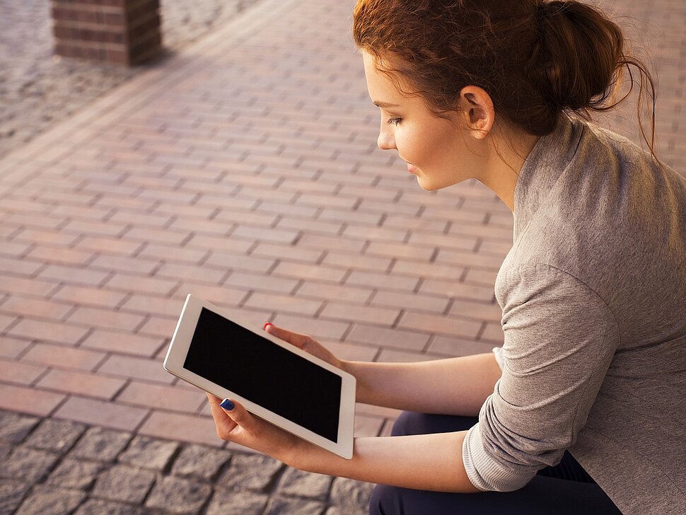 Das Bild zeigt eine Frau, die ein Tablet in der Hand hält.