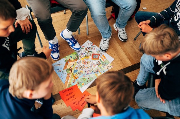 Fairtrade-Schüler:innen-Akademie Schüler:innen sitzen um einer Karte herum wo sie begriffe wie zum Beispiel Tierfreundliches Essen und Sportkleidung tauschen einsortieren.