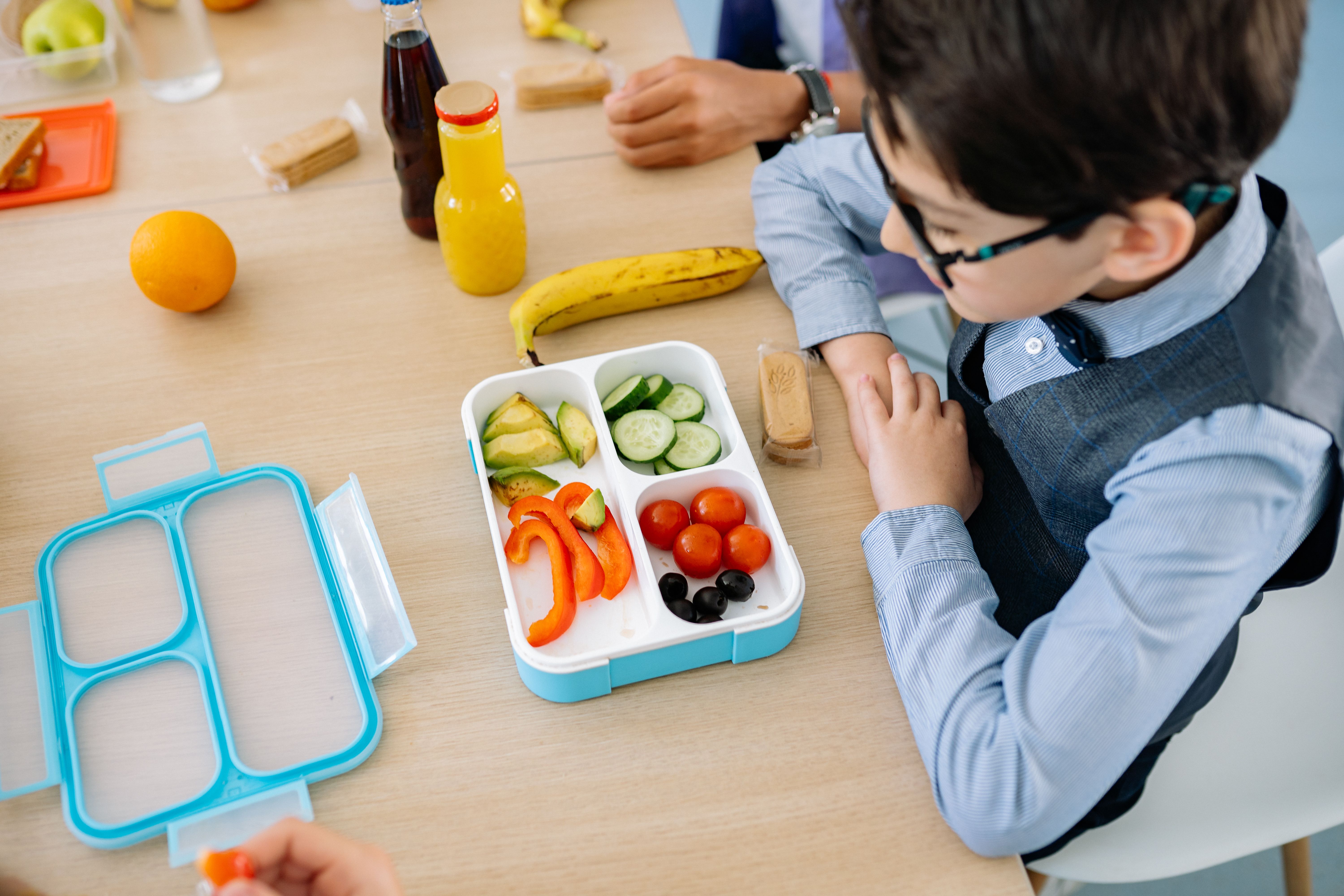 Nachhaltig snacken Ein Junge sitz vor einer Brotbox die mit verschiedenem Gemüse gefüllt ist.