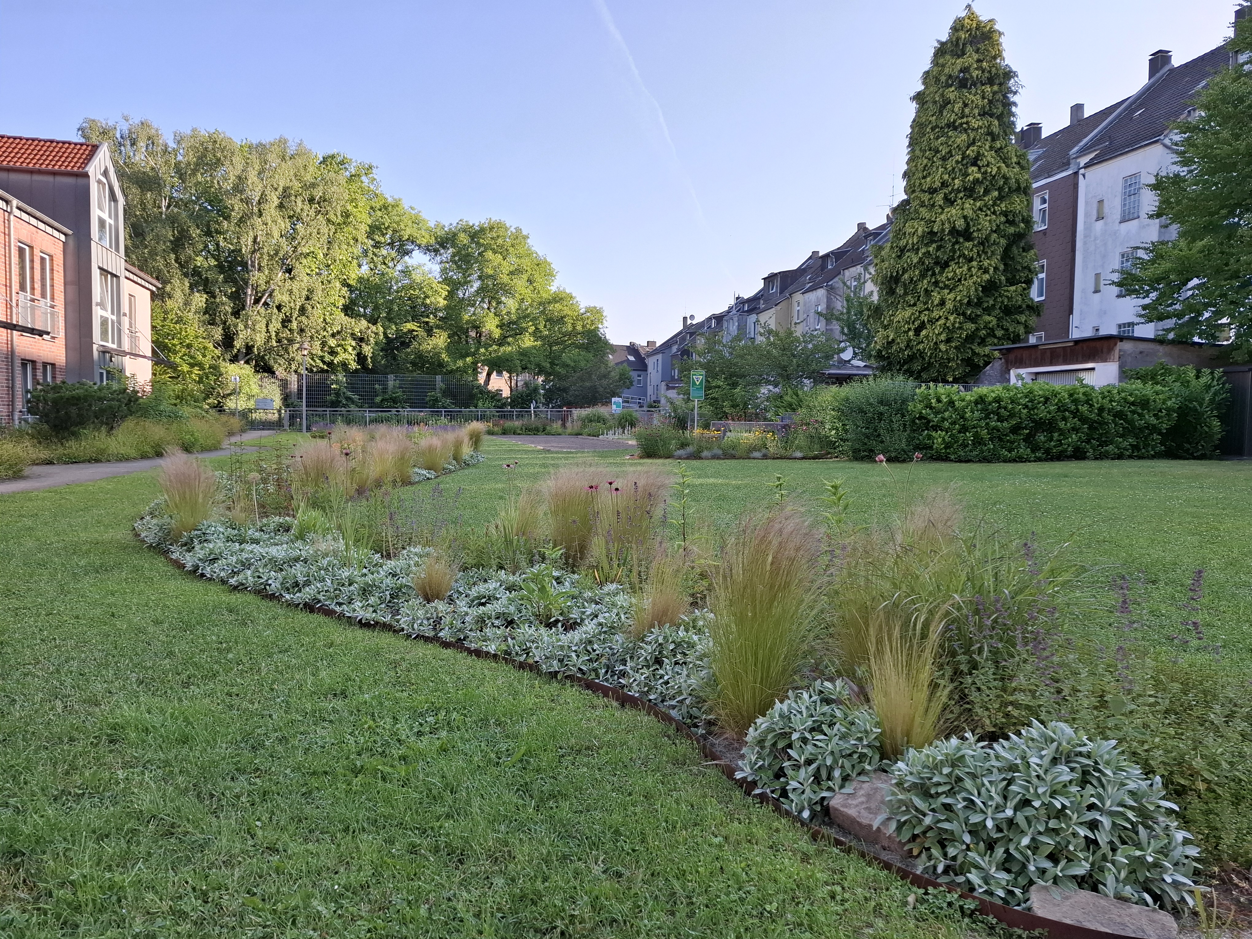 Für Anwohner*innen nutzbare Grünfläche inmitten von Wohnbebauung mit Blumenstreifen