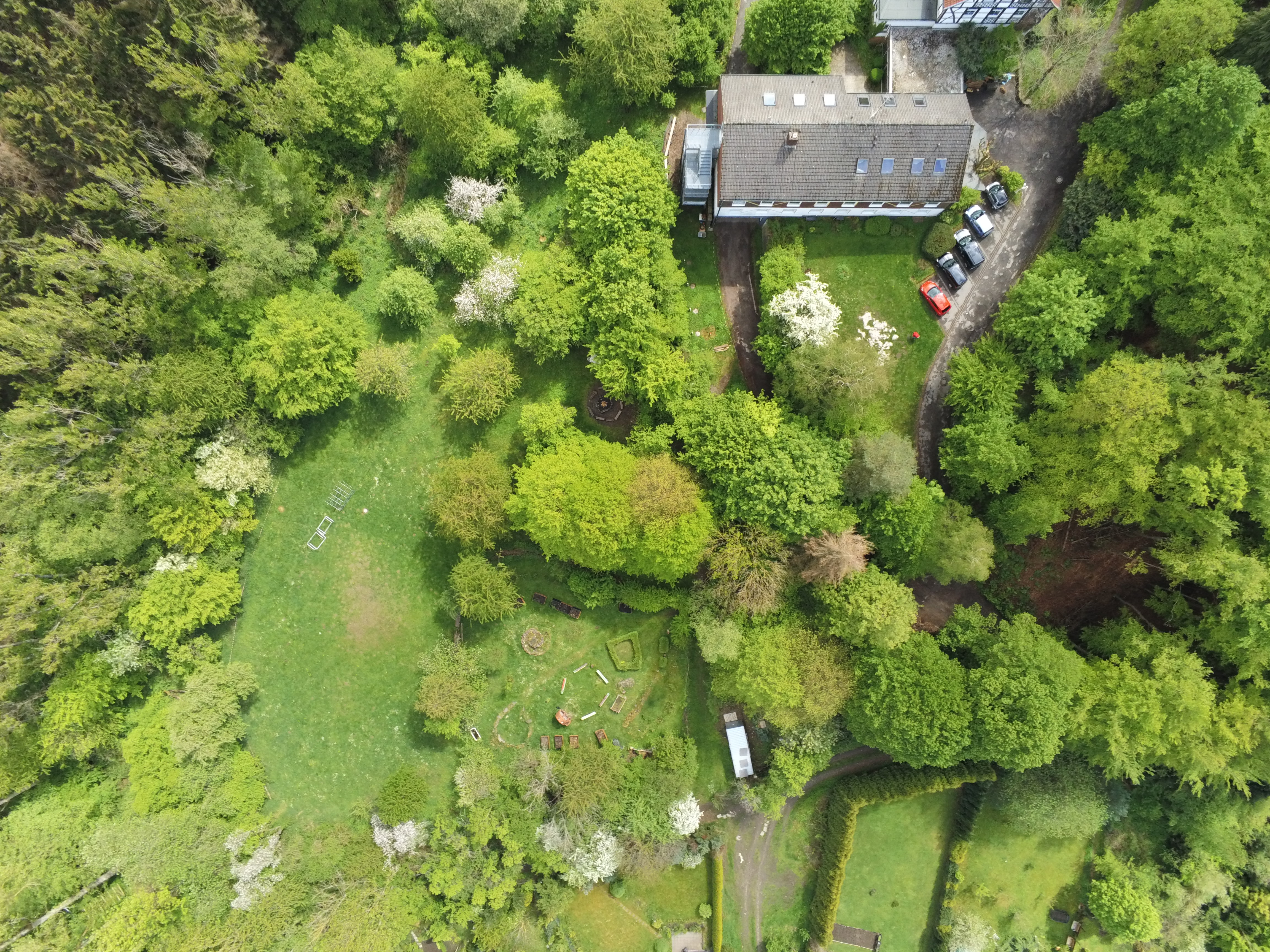 Blick aus dem Himmel auf grüne Rasen und Baumfläche. Dachfläche des Hauses ist etwas zu sehen