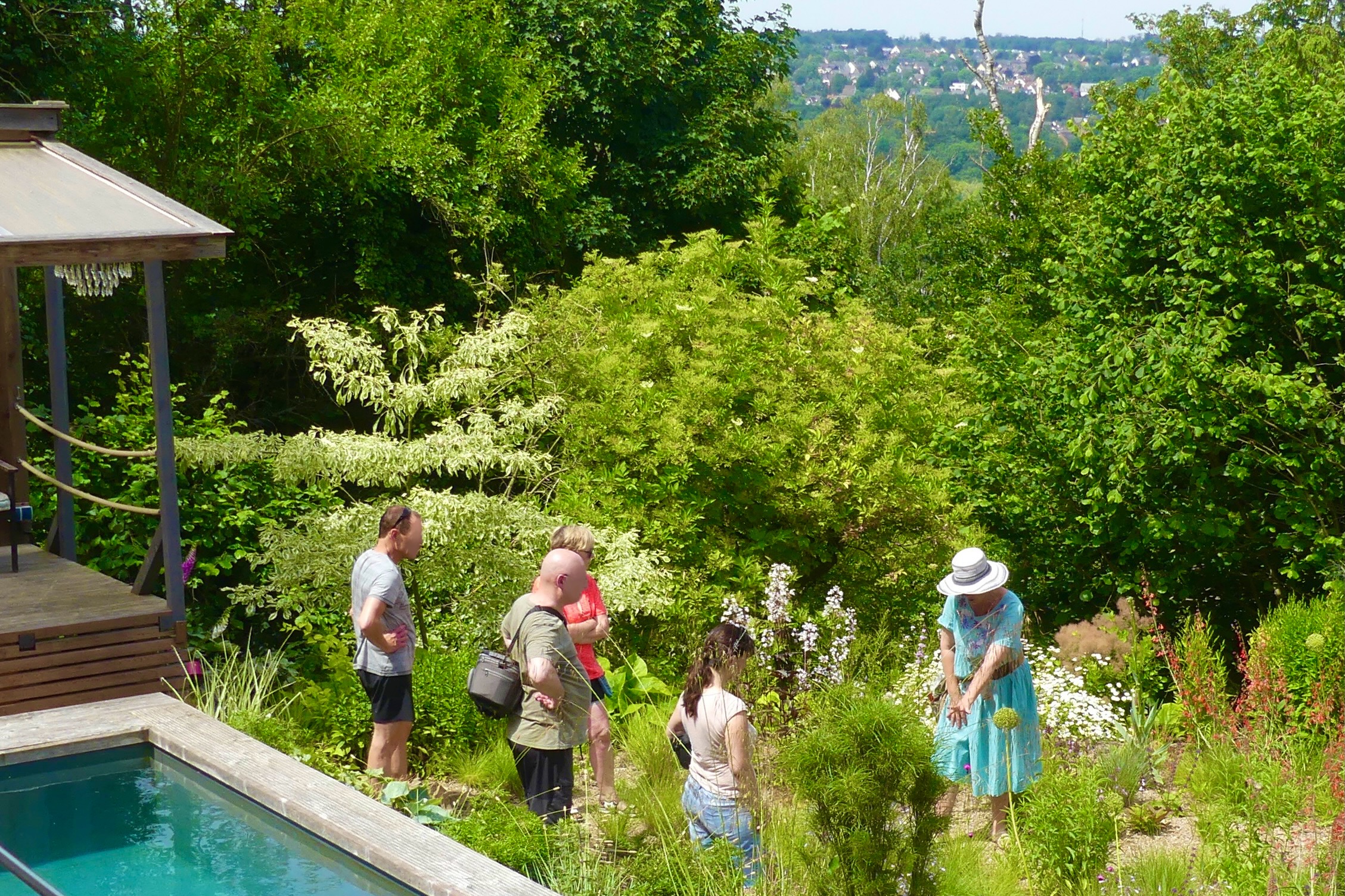 Hochsommerliche Stimmung: Die Gartenbesitzerin Eveline Hagemann mit Strohhut erklärt während der Offenen Gartenpforte (Gärten an der Ruhr), wie eine trockenheitsverträgliche Pflanzung im Splittbeet funktioniert. Sie steht dabei im Beet und 4 Besucher:innen stehen auf einem Weg direkt in ihrer Nähe und hören zu.
