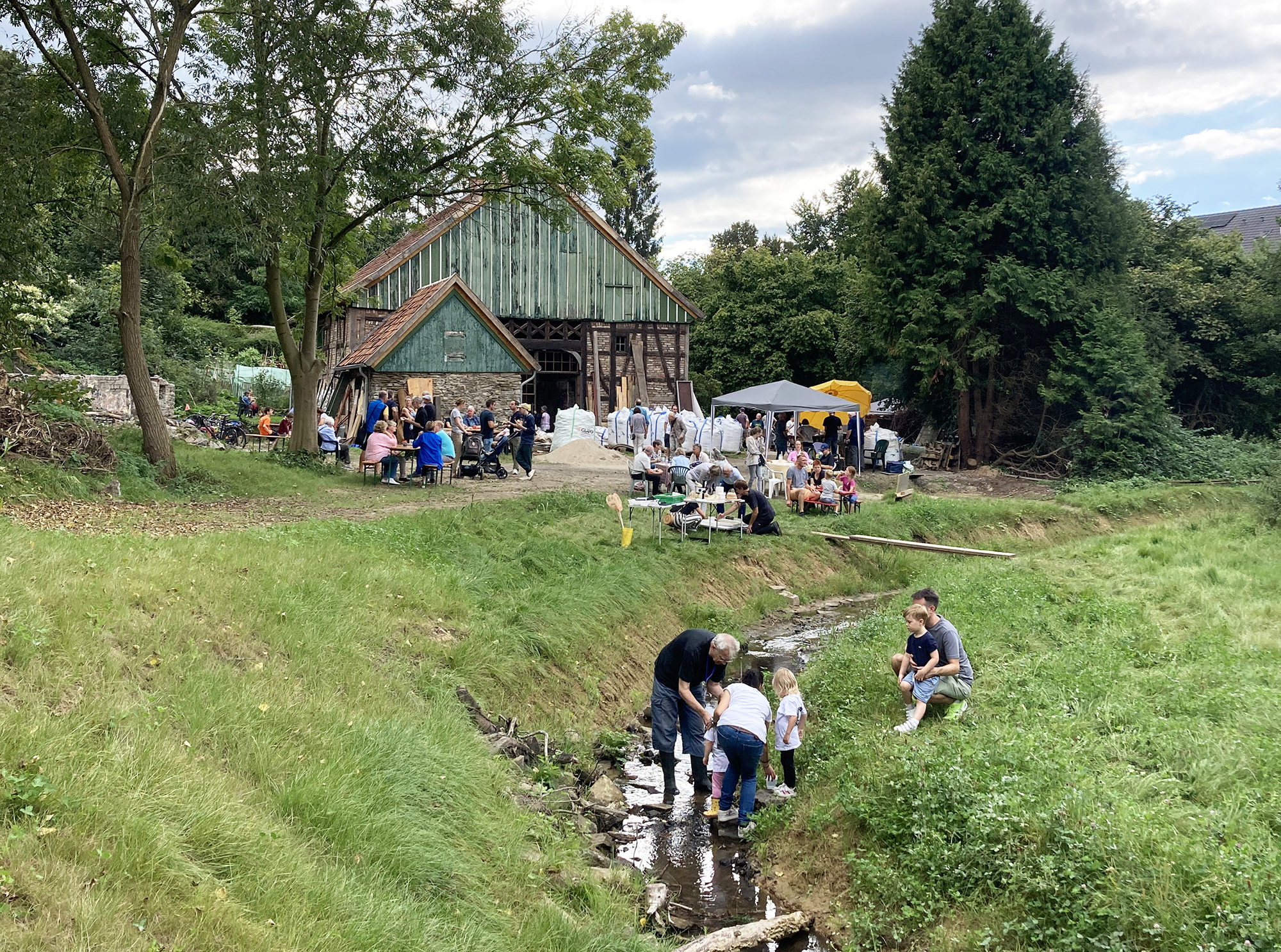 Günnemann-Kotten, Witten Der Bach Brunebecke hat ein neues Beet bekommen. Erwachsene und Kinder suchen im Wasser nach Kleinstlebewesen. Im Hintergrund sieht man den historischen Günnemann-Kotten.