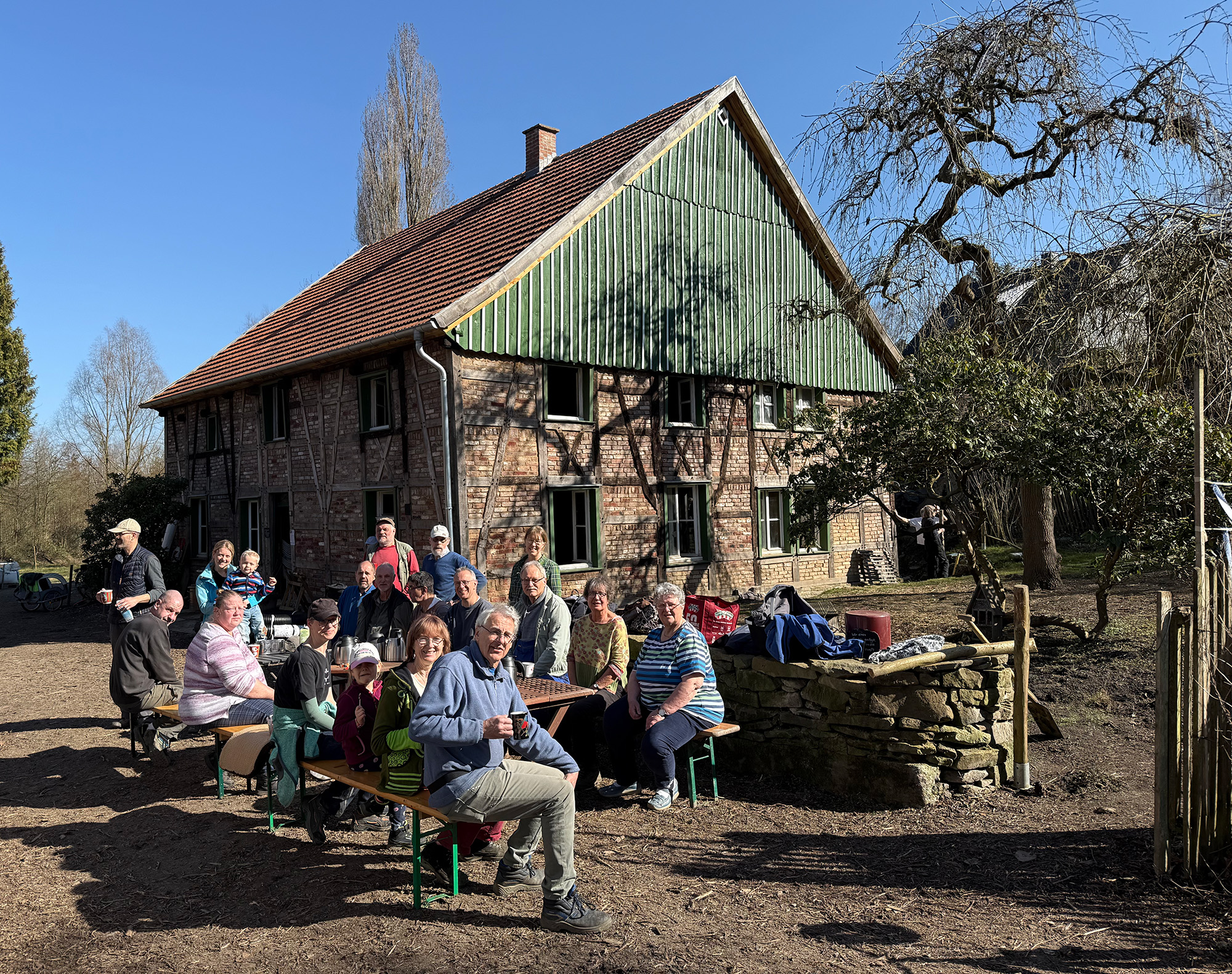 Günnemann-Kotten, Witten Eine Gruppe Menschen unterschiedlichen Alters sitzt in der Sonne an Bierbänken. Im Hintergrund sieht man den historischen Günnemann-Kotten.