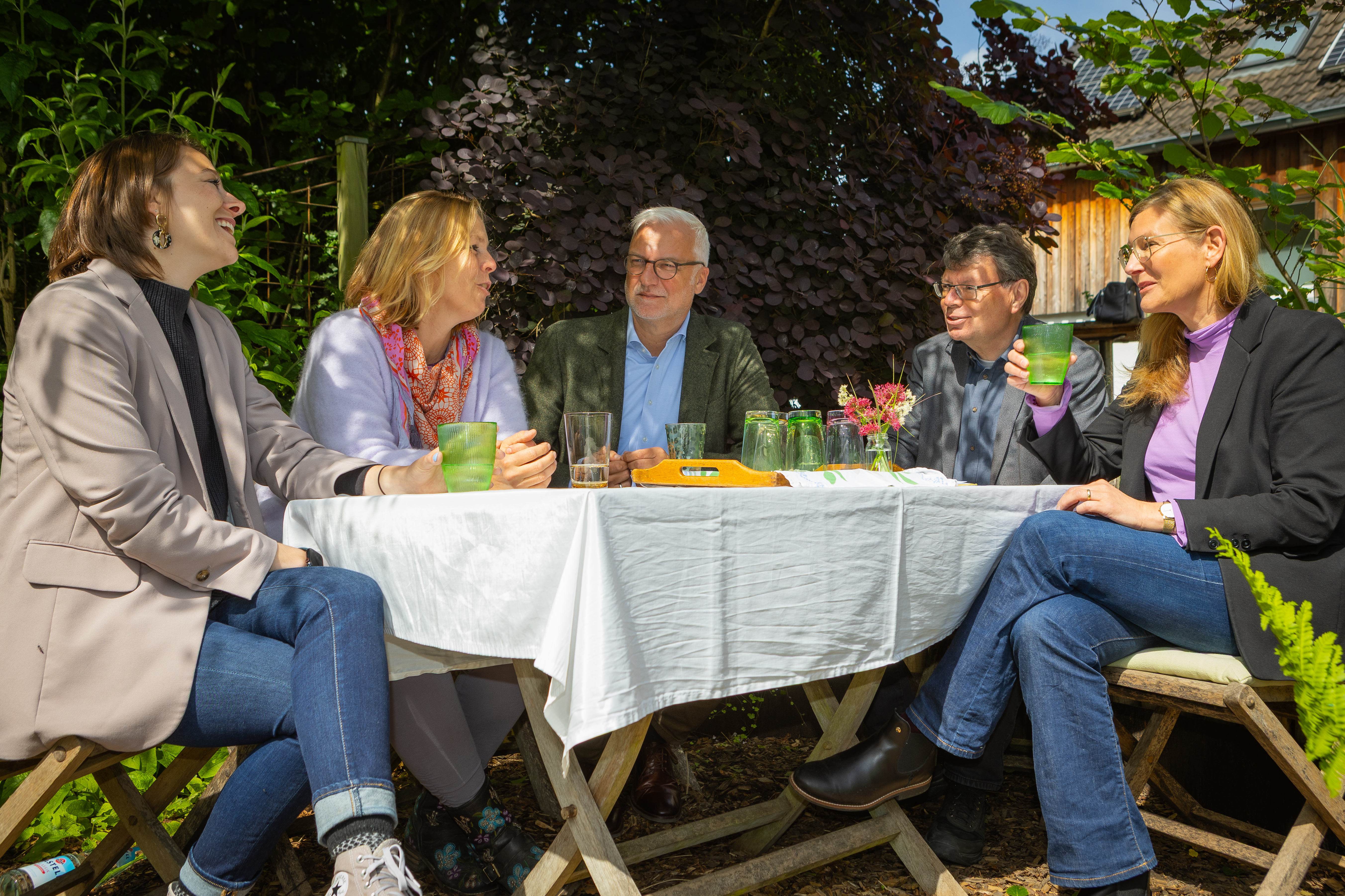 Fünf Personen unterhalten sich an einem Tisch in einem Garten.