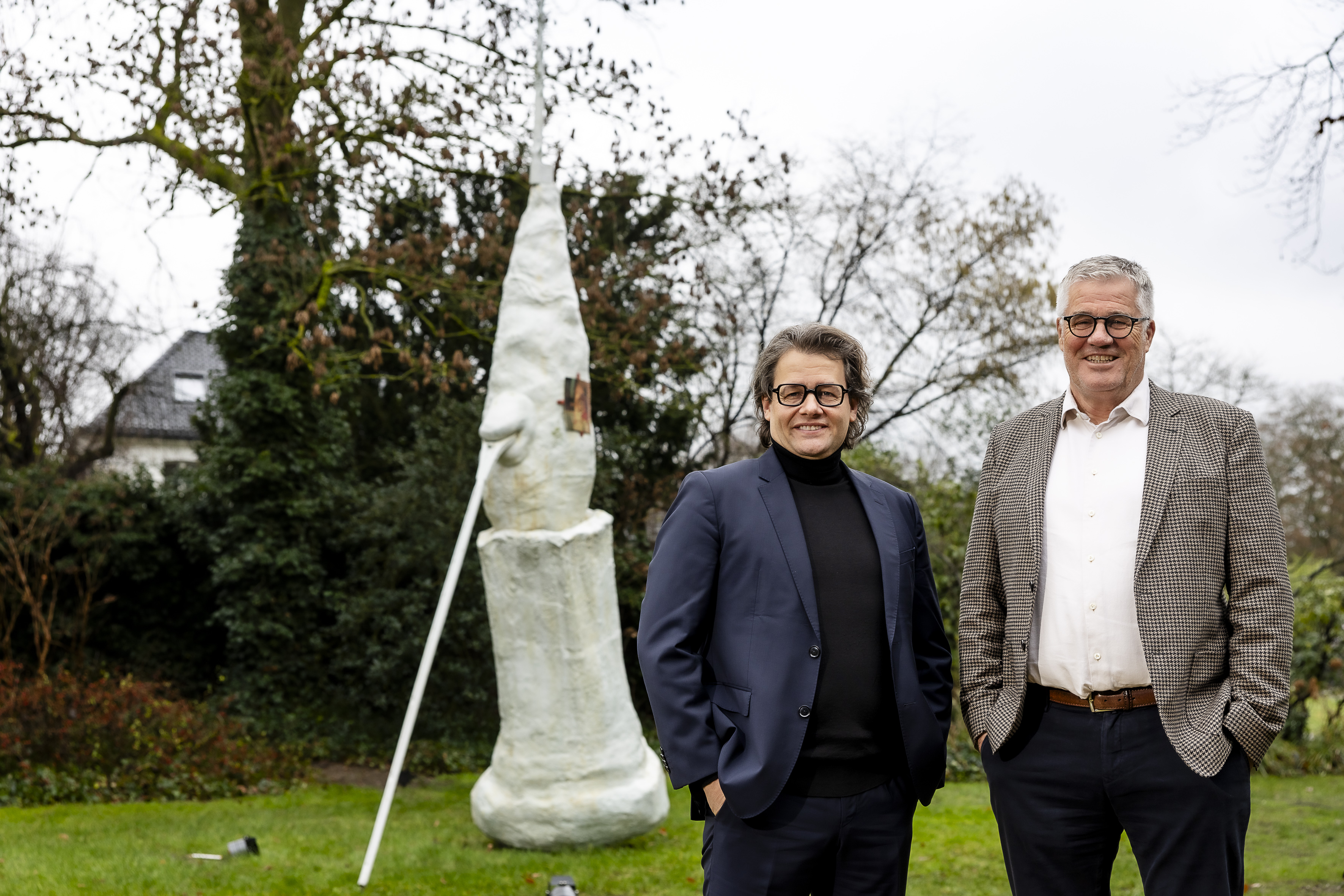 Zwei Männer nebeneinander vor einer Skulptur in einem Park