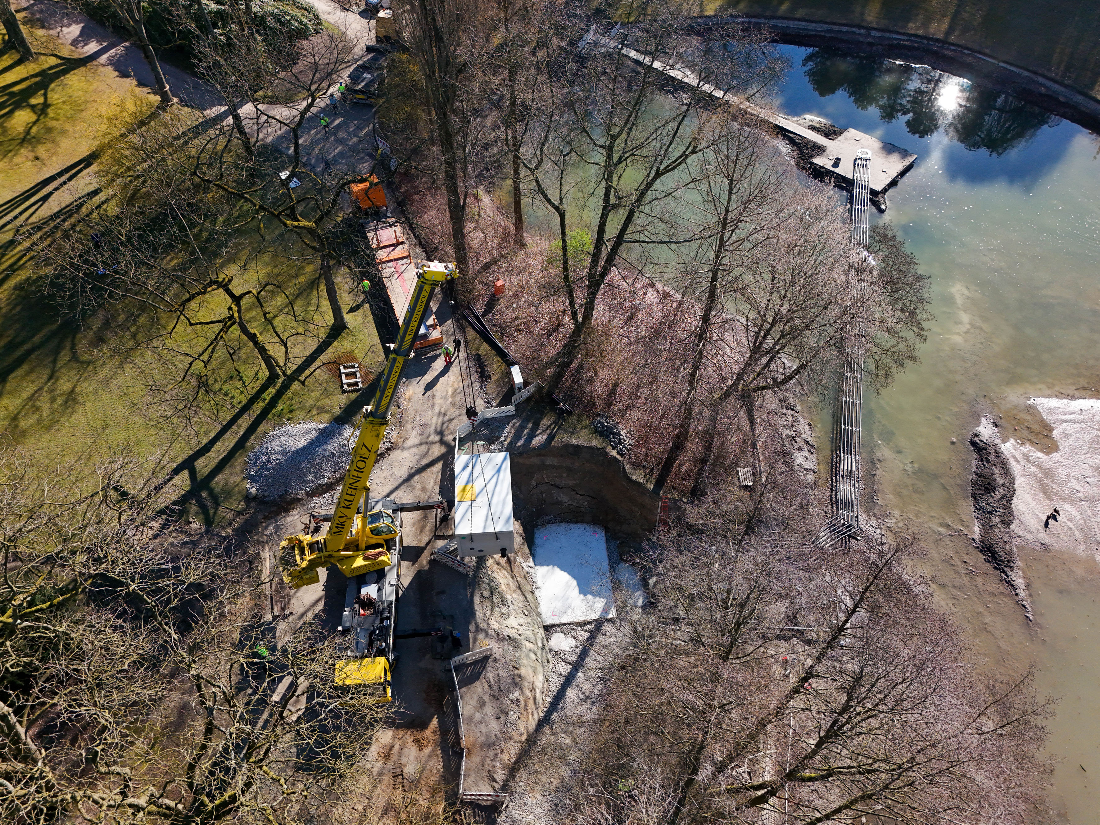 Gelber Kran mit Wasser zur rechten Seite und Wiese zur linken.