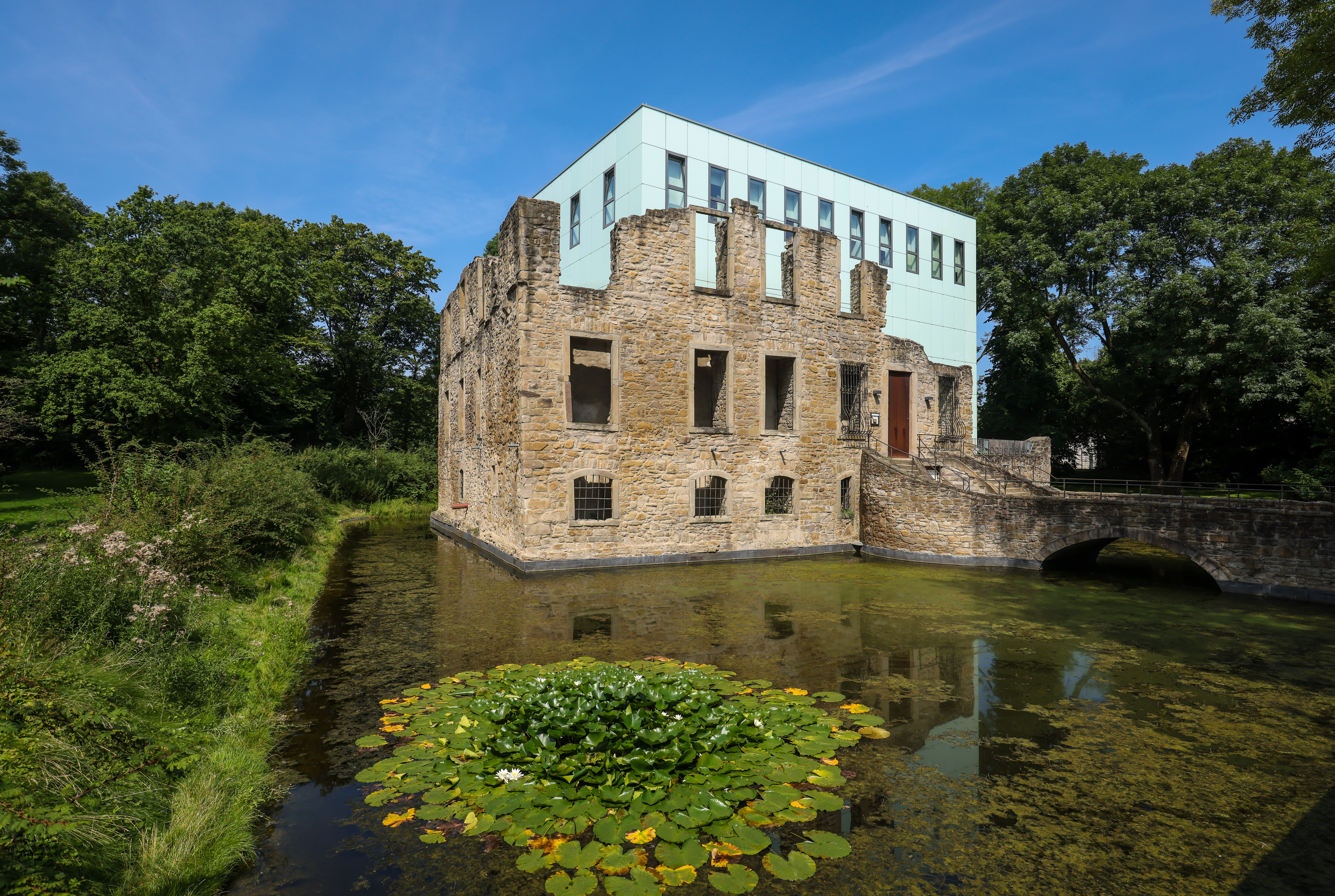 Gebäude mit Brücke umgeben von Wasser, Seerosen und Bäumen