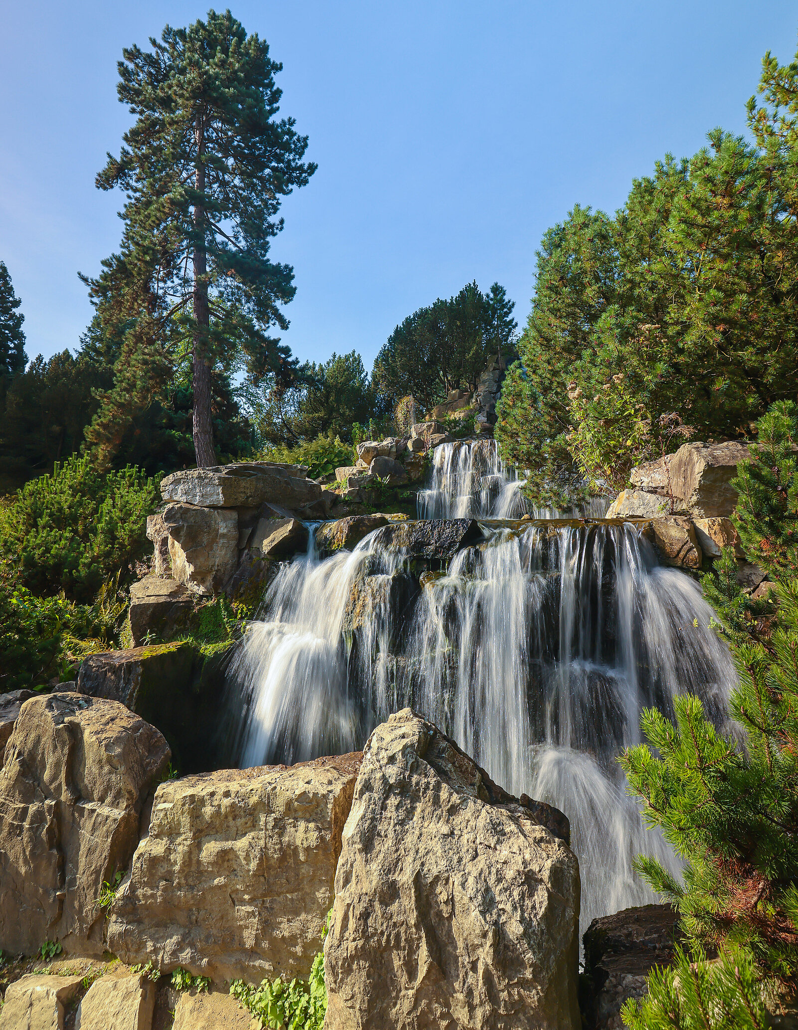 Ein mehrstöckiger Wasserfall umgeben von Felsen und weiteren Bäumen