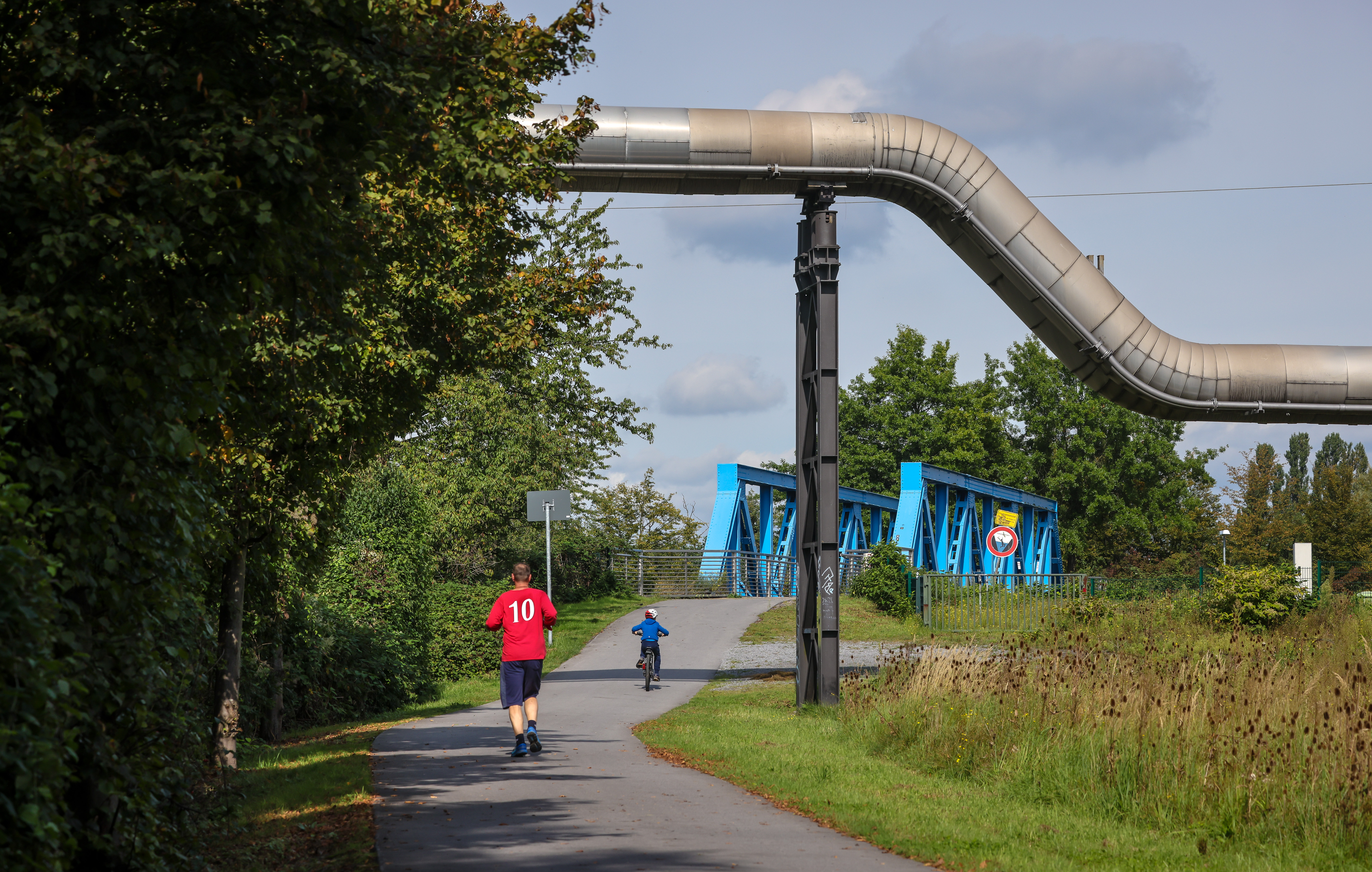 Ein Jogger und ein Rad fahrendes Kind auf dem Weg zu einer blauen Brücke