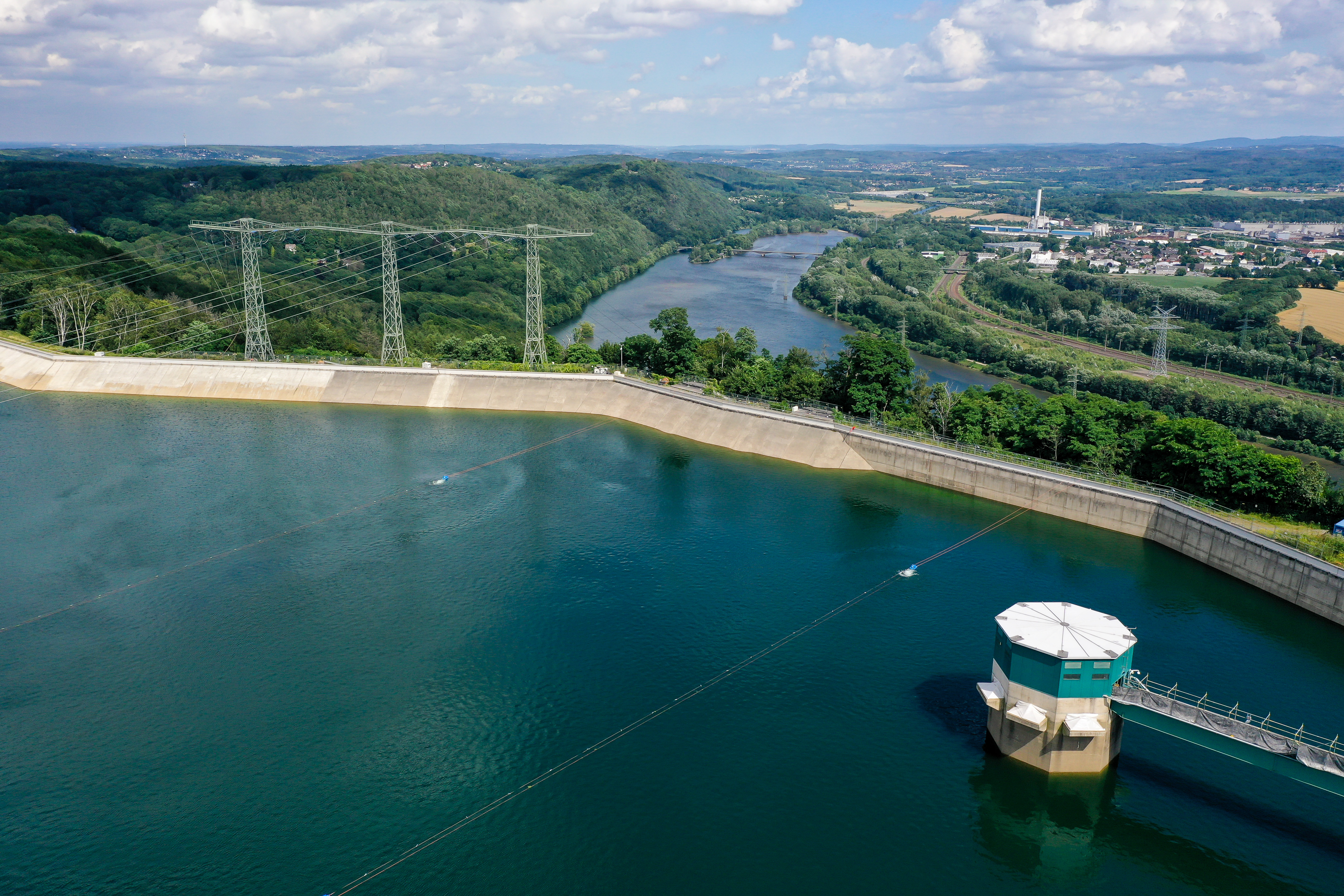 Im Vordergrund gestautes Wasser hinter der Mauer. Im Hintergrund die Ruhr, Wälder und Wohnhäuser.
