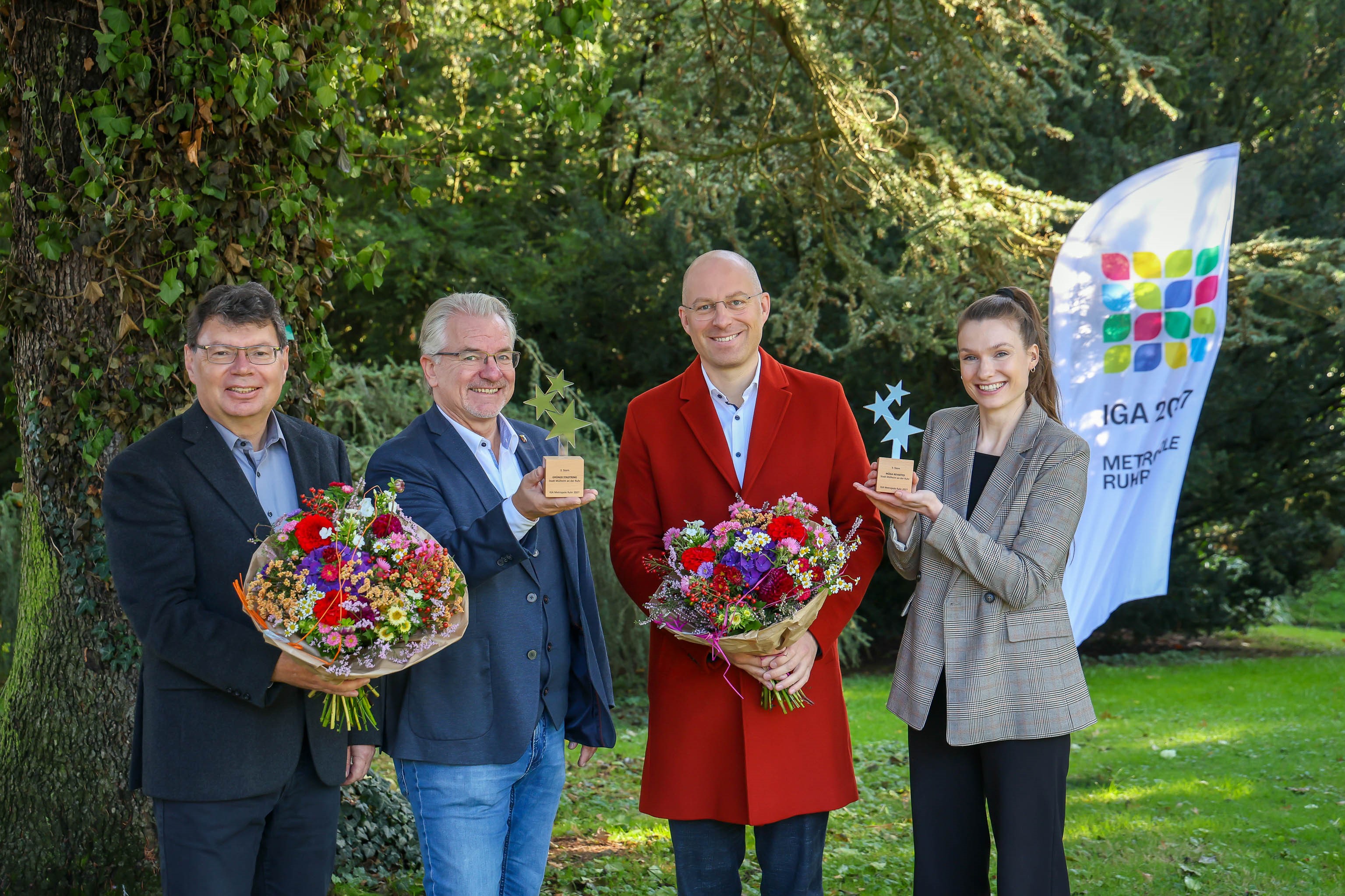 Vier Personen mit zwei Pokalen und zwei feierlichen Blumensträußen.