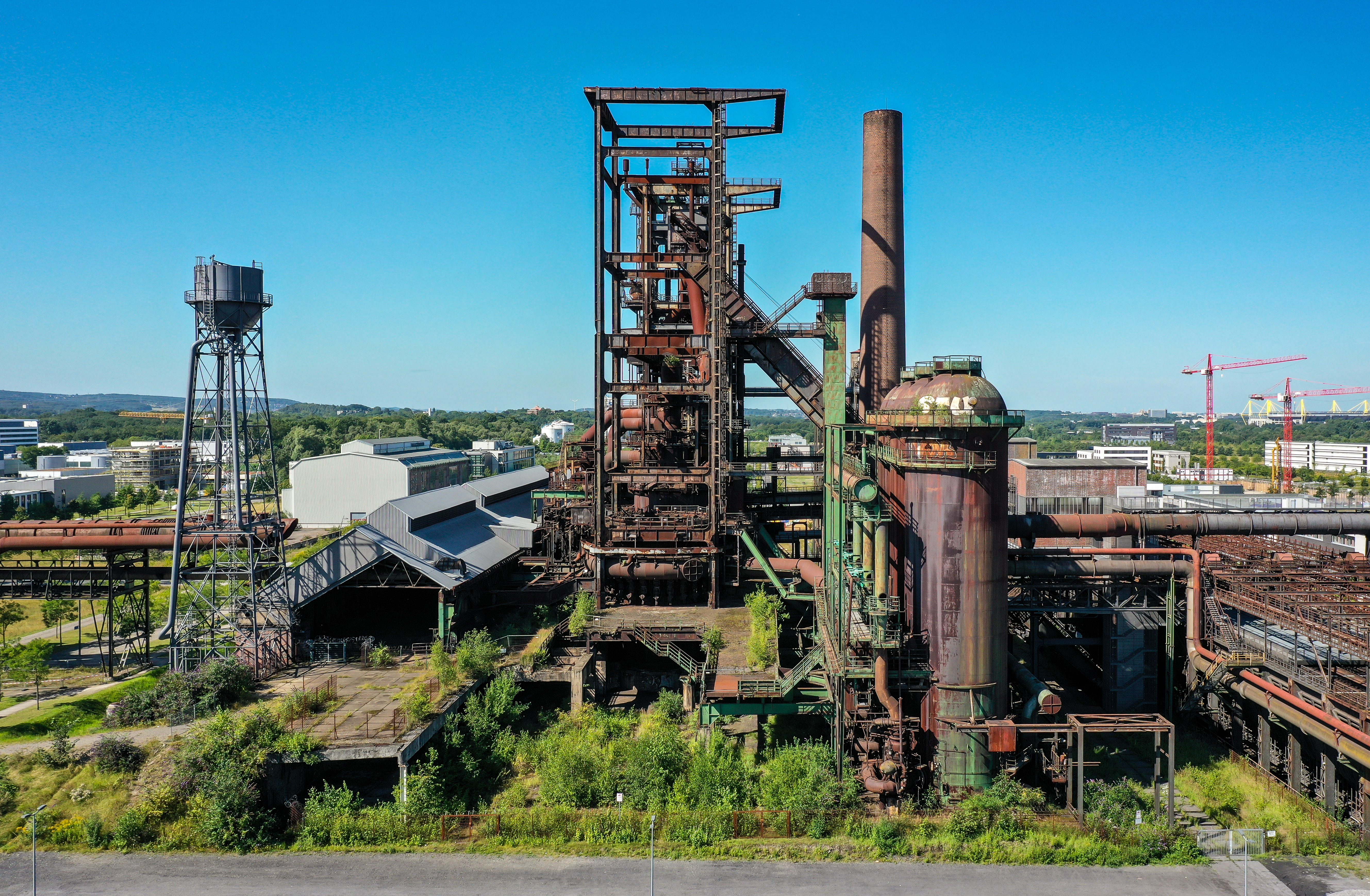 Hochofenwerk in der Mitte umgeben von Bäumen und weiter entfernt Häuser
