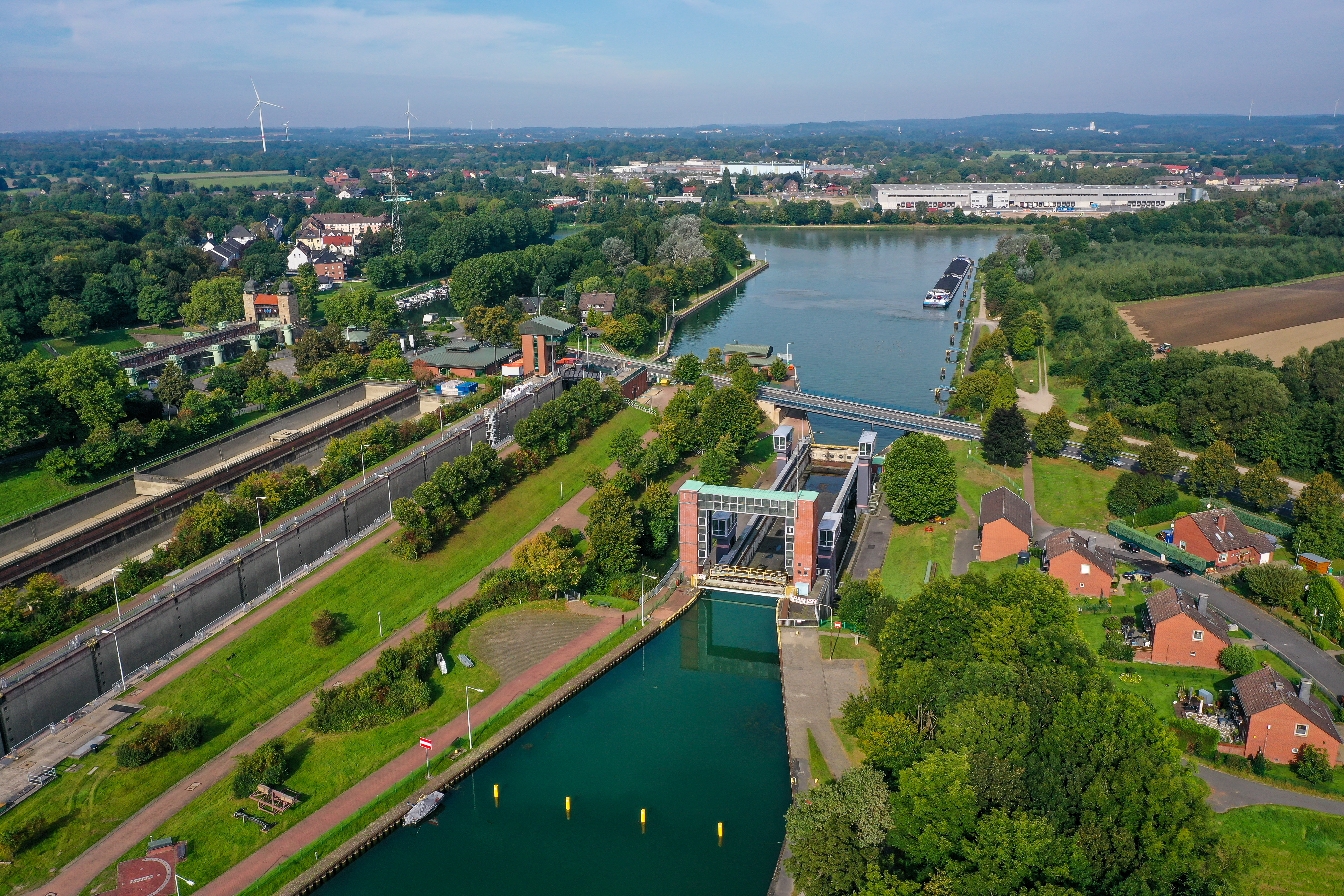 Vogelperspektive auf den Schleusenpark am Wasser, umgeben von grünen Bäumen und vereinzelt Häusern