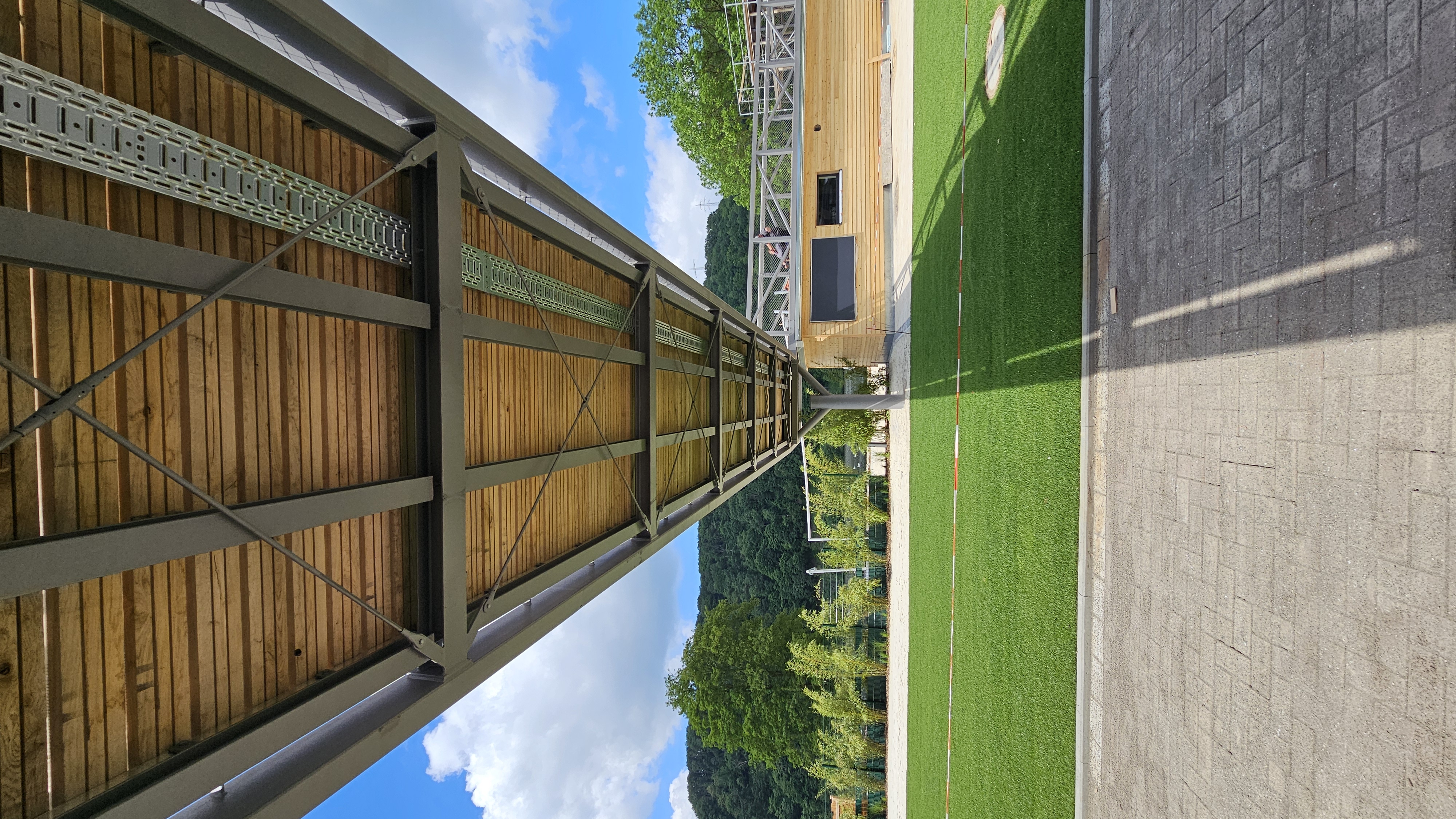 Blick auf einen Weg und grüne Wiese, aus der Perspektive unter dem Steg.