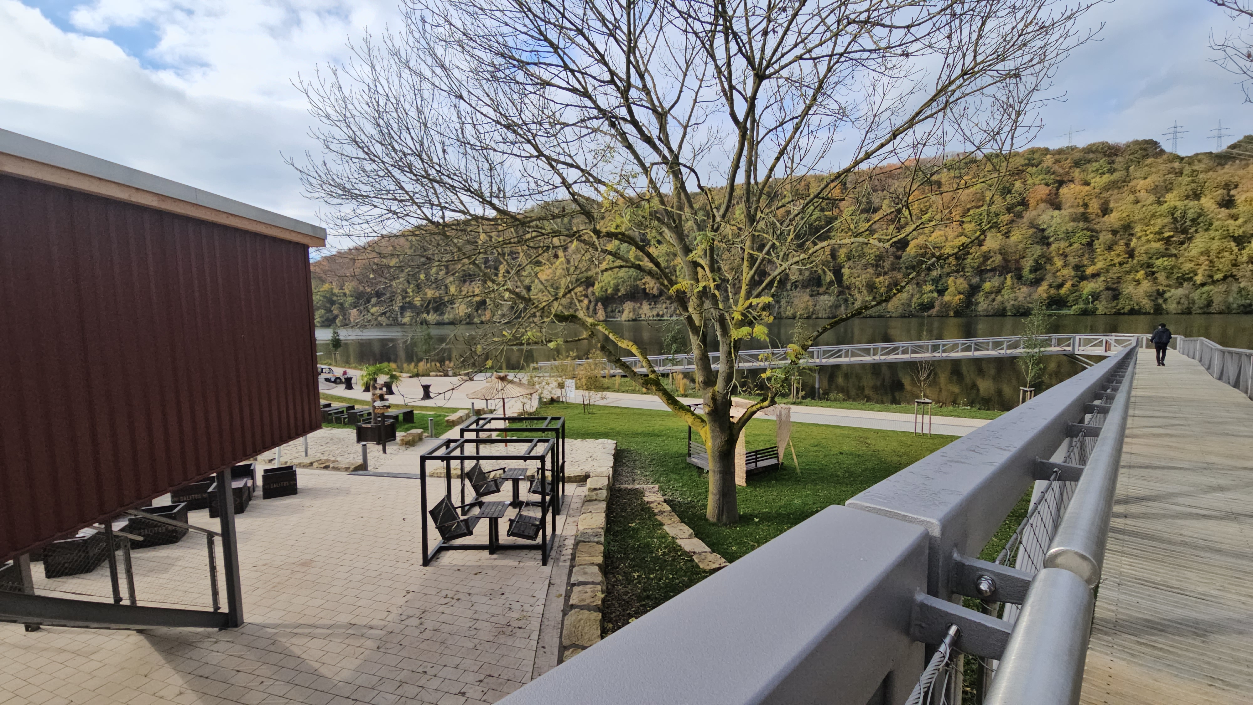 Blick vom Ufer und Steg aus auf den Steg am See. Im Hintergrund herbstliche Bäume
