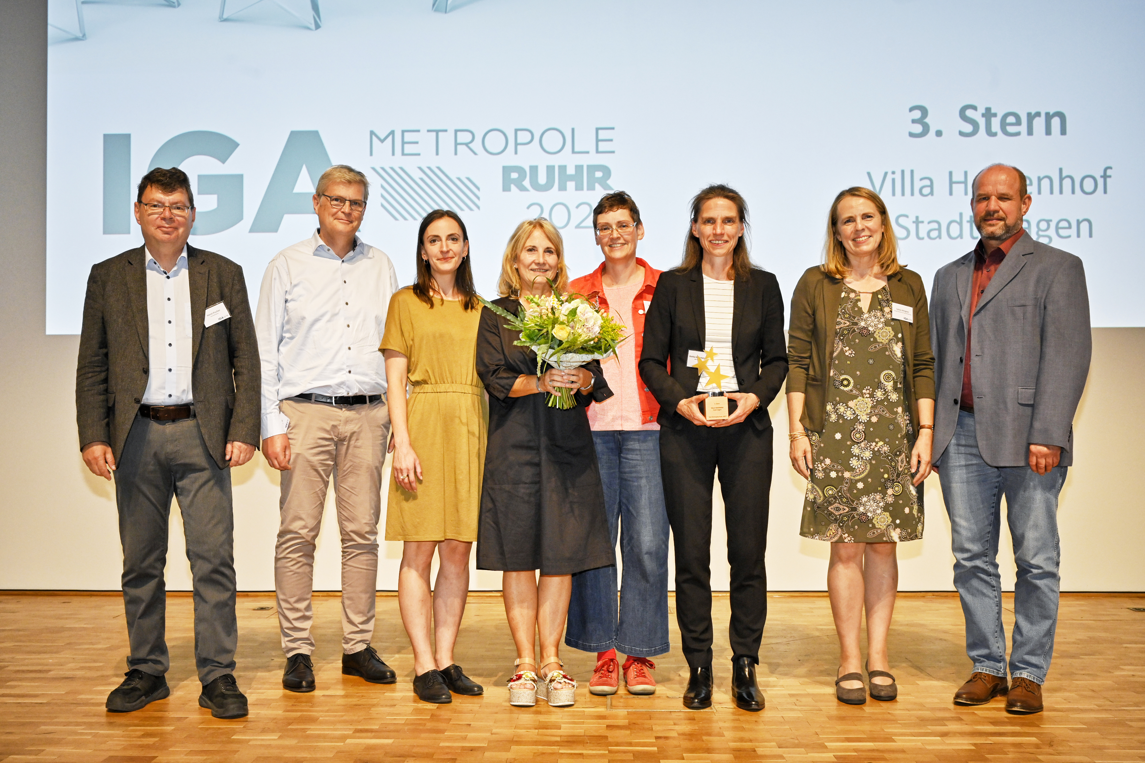 acht Personen bei der feierlichen Übergabe des dritten IGA Sterns, dahinter IGA Werbe Leinwand